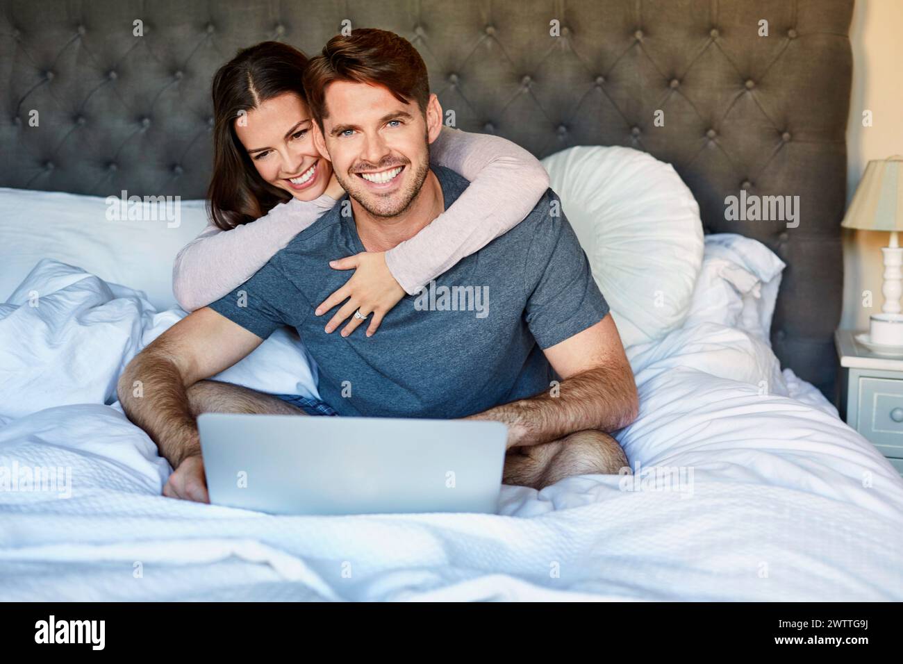 Couple smiling and using a laptop in bed Stock Photo