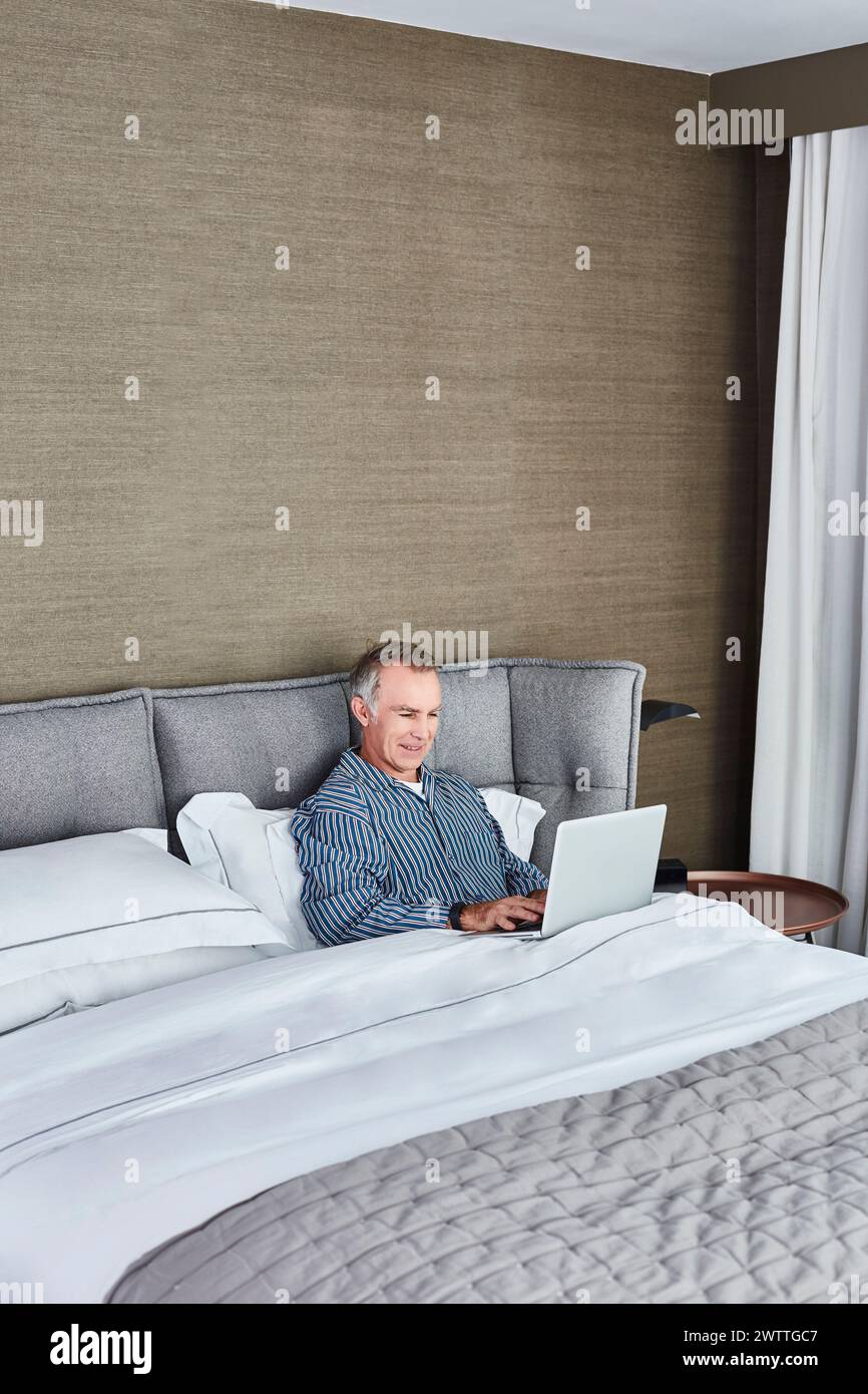 Man using laptop while sitting in bed Stock Photo