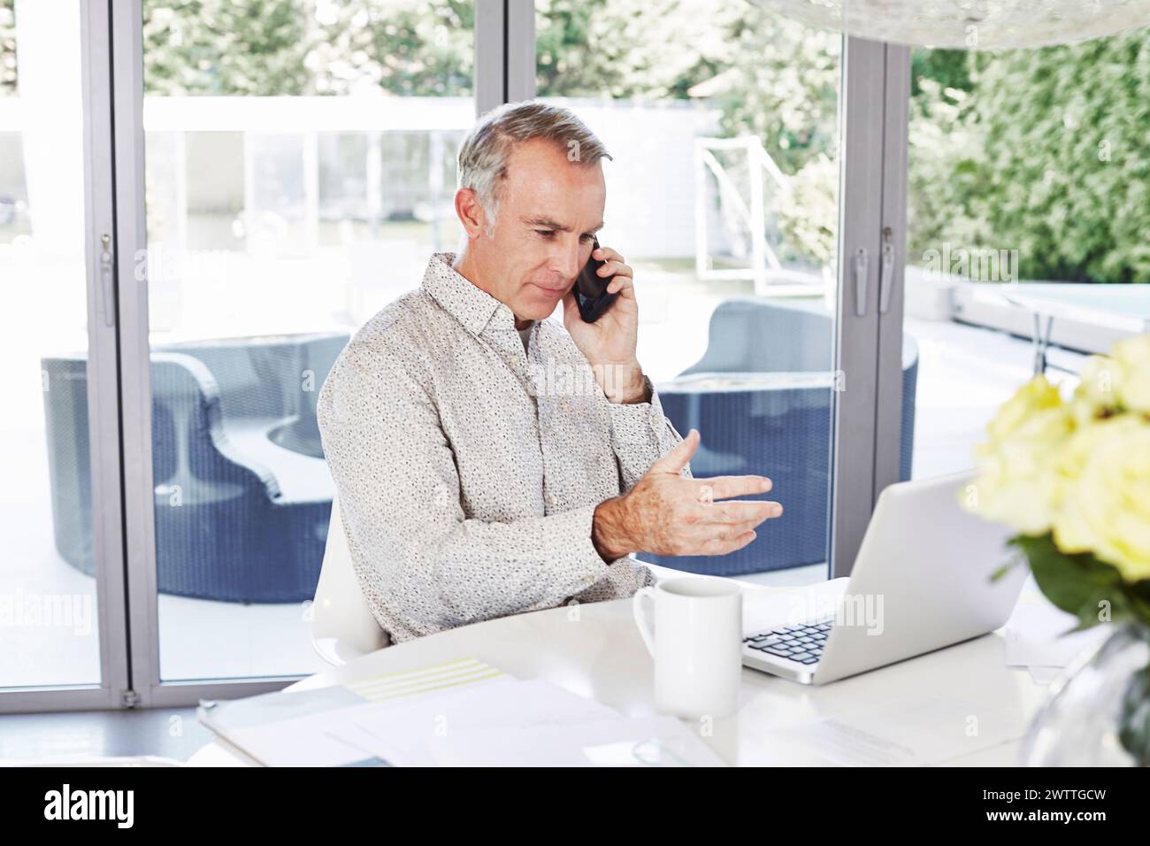 Man talking on phone while working on laptop at home Stock Photo