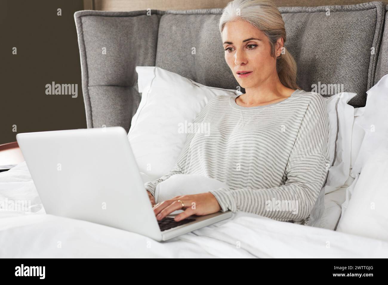 Woman working on laptop in bed Stock Photo