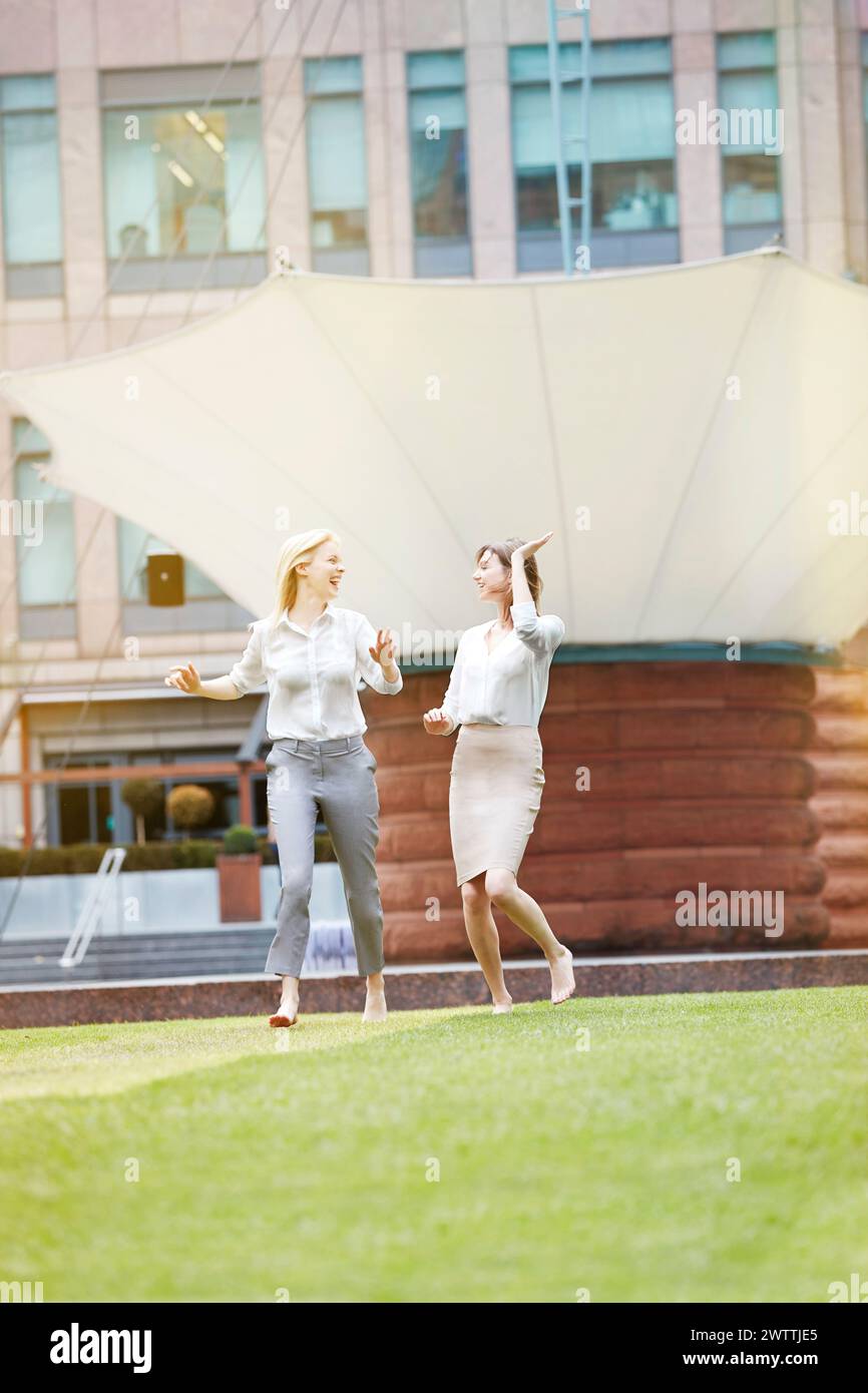Two women walking happily on grass with a building in the background. Stock Photo