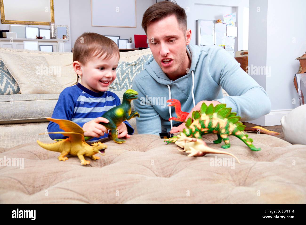 Adult and child playing with dinosaur toys on a sofa Stock Photo
