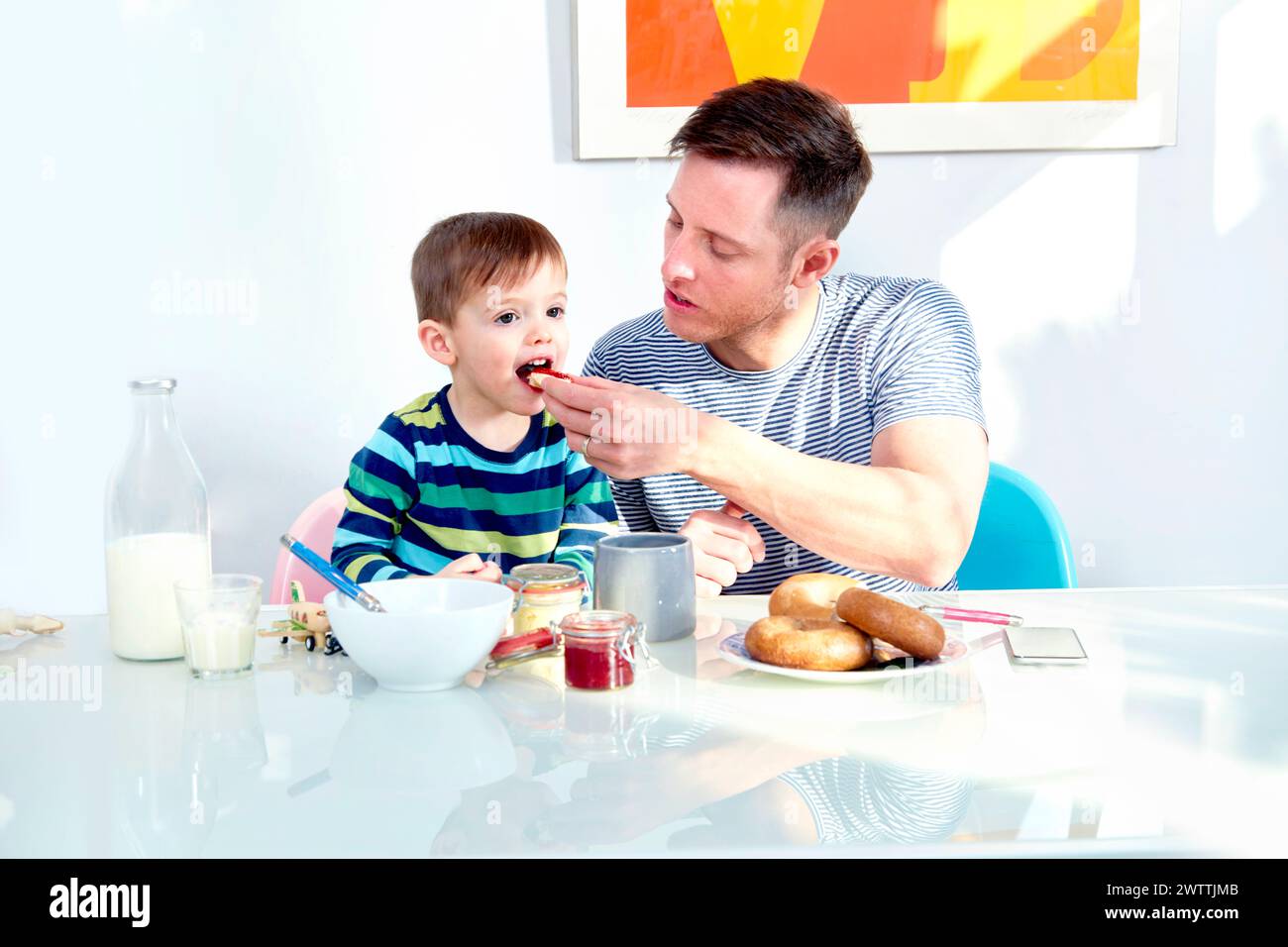 Father feeding toddler at breakfast table Stock Photo