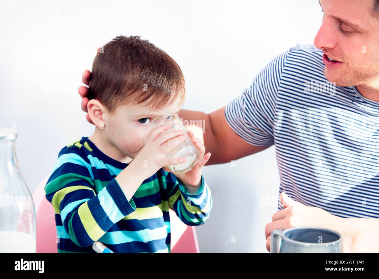 Boy drinking milk with an adult by his side. Stock Photo