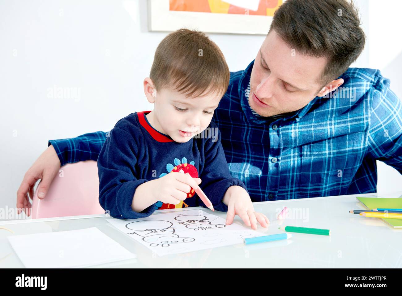Adult assisting a child with coloring at a table. Stock Photo