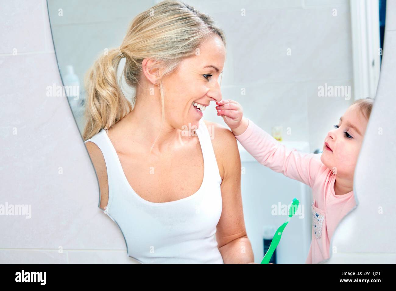 Toddler brushing mother's teeth in bathroom Stock Photo
