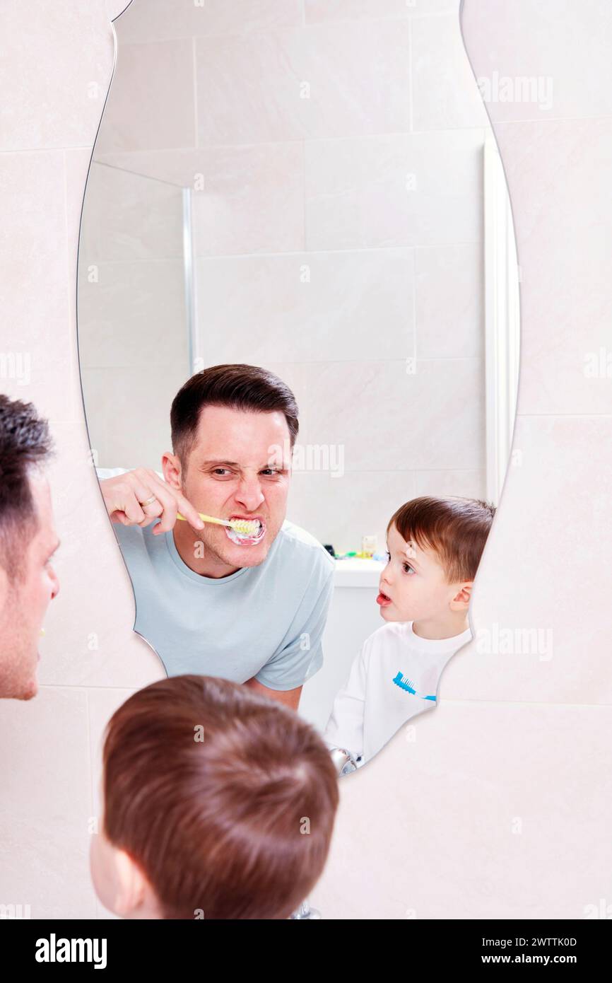 Man and child brushing teeth together in mirror reflection Stock Photo