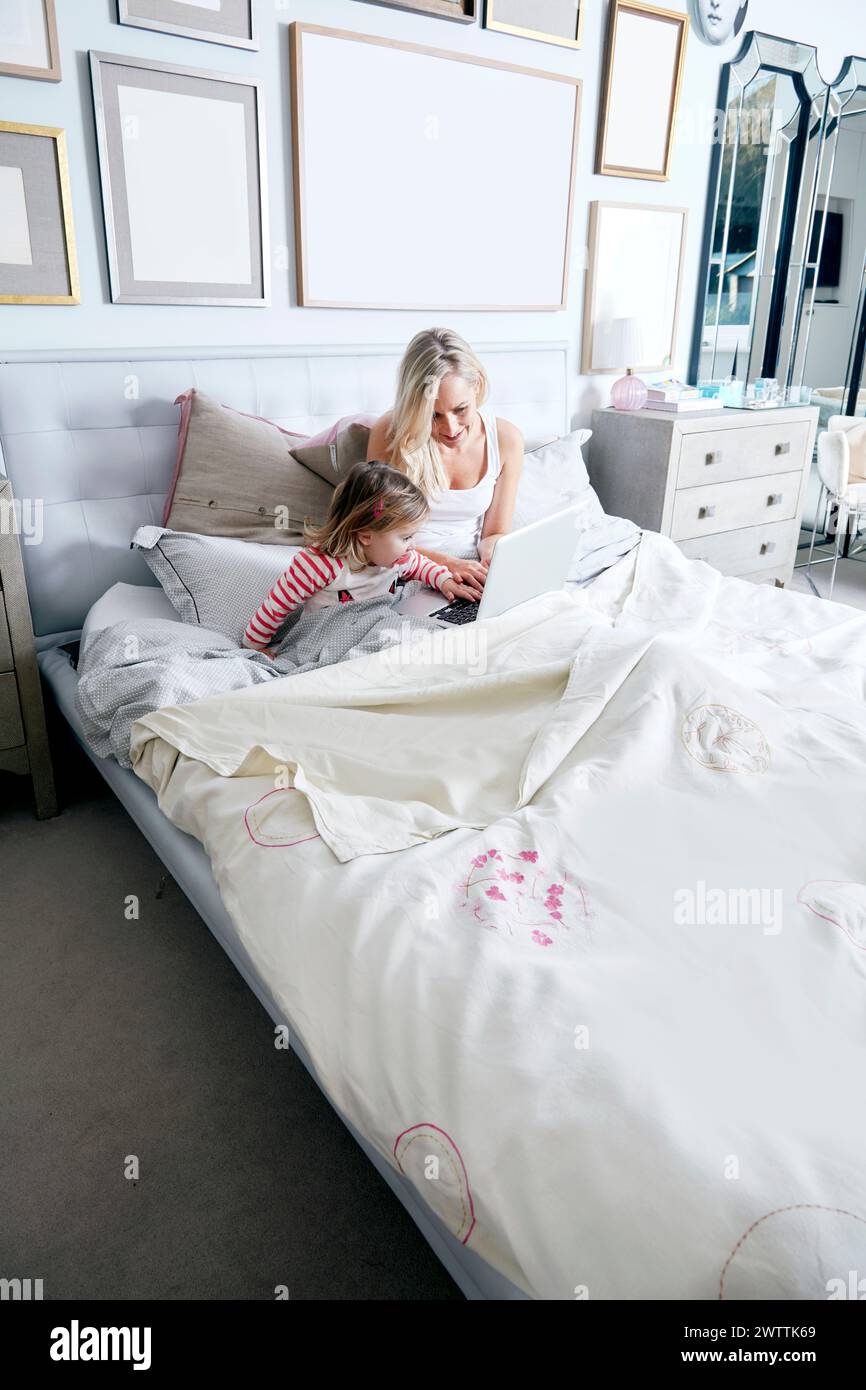 Woman and child using laptop on bed. Stock Photo