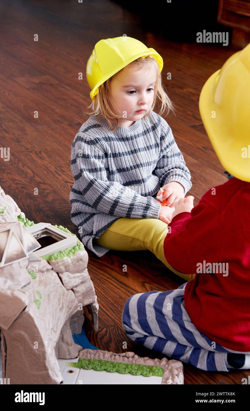 Toddler in a yellow hard hat playing with another child Stock Photo