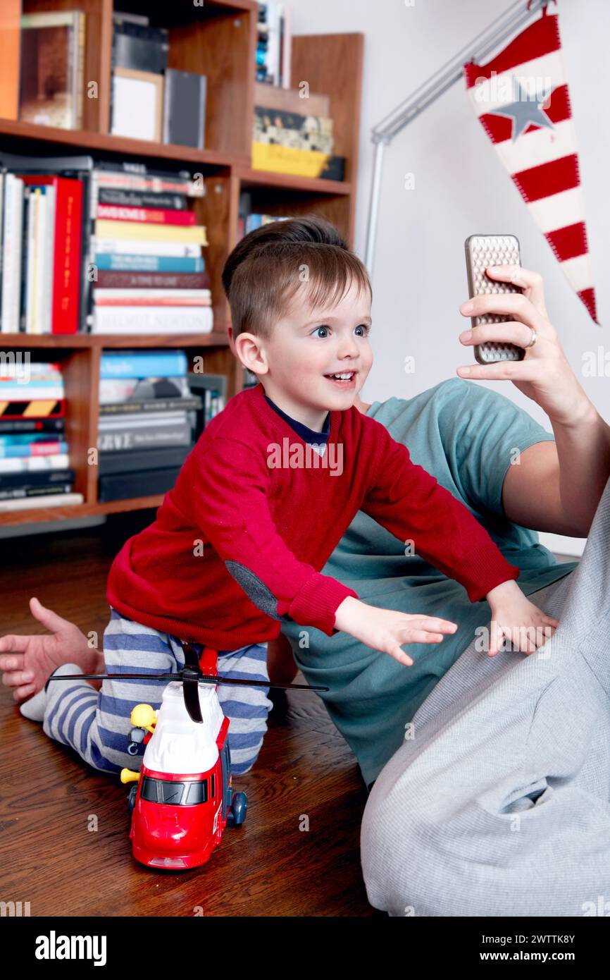 Child playing with toy firetruck and reaching for a smartphone. Stock Photo