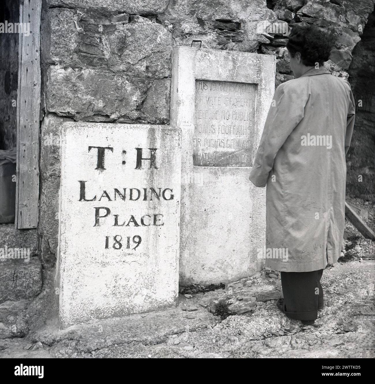 1950s, historical, on Lundy Island, a lady standing at two ancient granite  monuments. One statesl T:H Landing Place 1819. The other, taller one, has an engraving..... This Island Is Private Property..No Public Roads Or Footpaths. Lying in the Bristol Channel, off the coast of North Devon, the small Island of Lundy - literally puffin as from the bird - has many ancient monuments and listed buildings and is only accessible by boat. Stock Photo