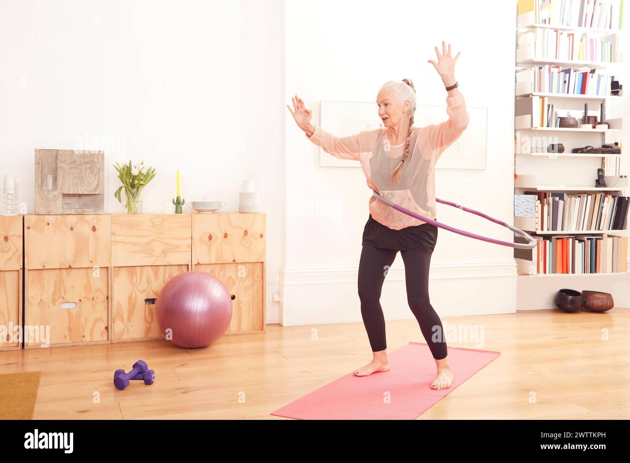 Elderly woman exercising with a hula hoop indoors Stock Photo