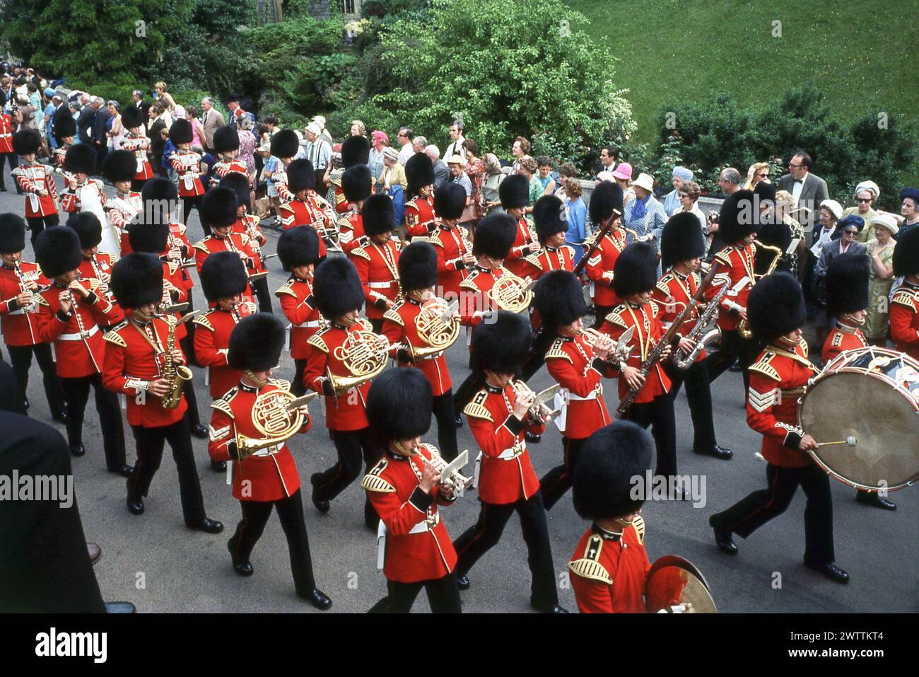 1960s, historical, view from above of the band of the Grenadier Guards in full dress uniform and traditional fur cap, known as bearskins, playing their instruments as they march at the Order of the Garter and Procession event at Windsor Castle, Berkshjire, England, UK. One of the oldest and most famous military bands, with a long history, dating back to 1665, the band, as part of the Bands of the Household Division, plays at important British ceremonial and royal events. Stock Photo