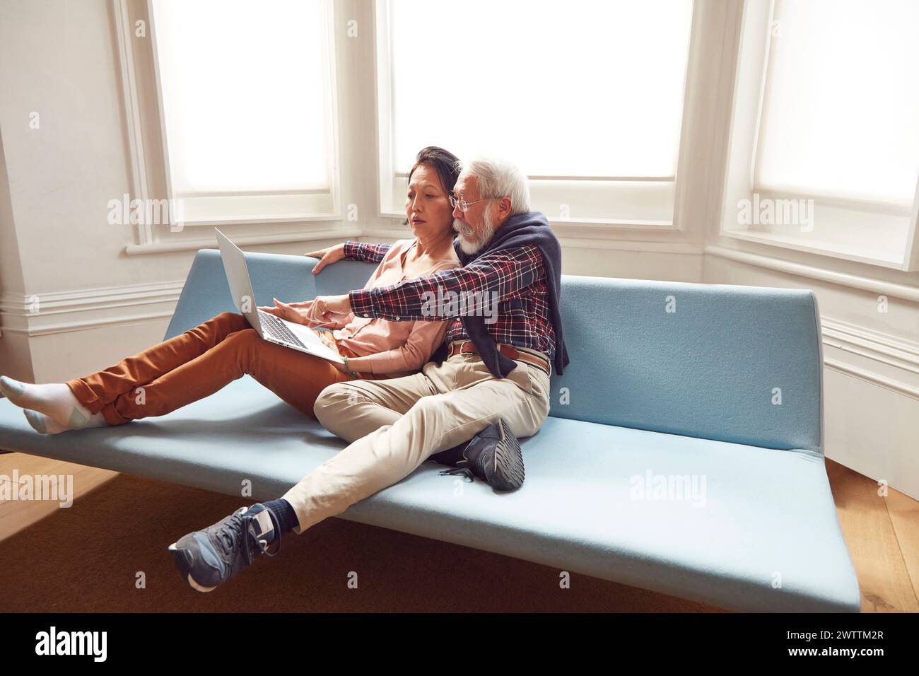 Elderly couple using a laptop on a blue sofa Stock Photo