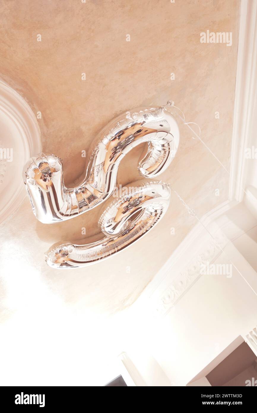 Silver balloon in the shape of the number five floating indoors Stock Photo