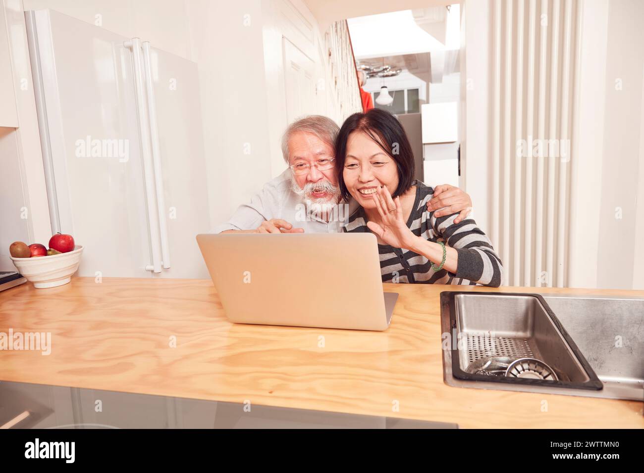Elderly couple using a laptop in a kitchen. Stock Photo