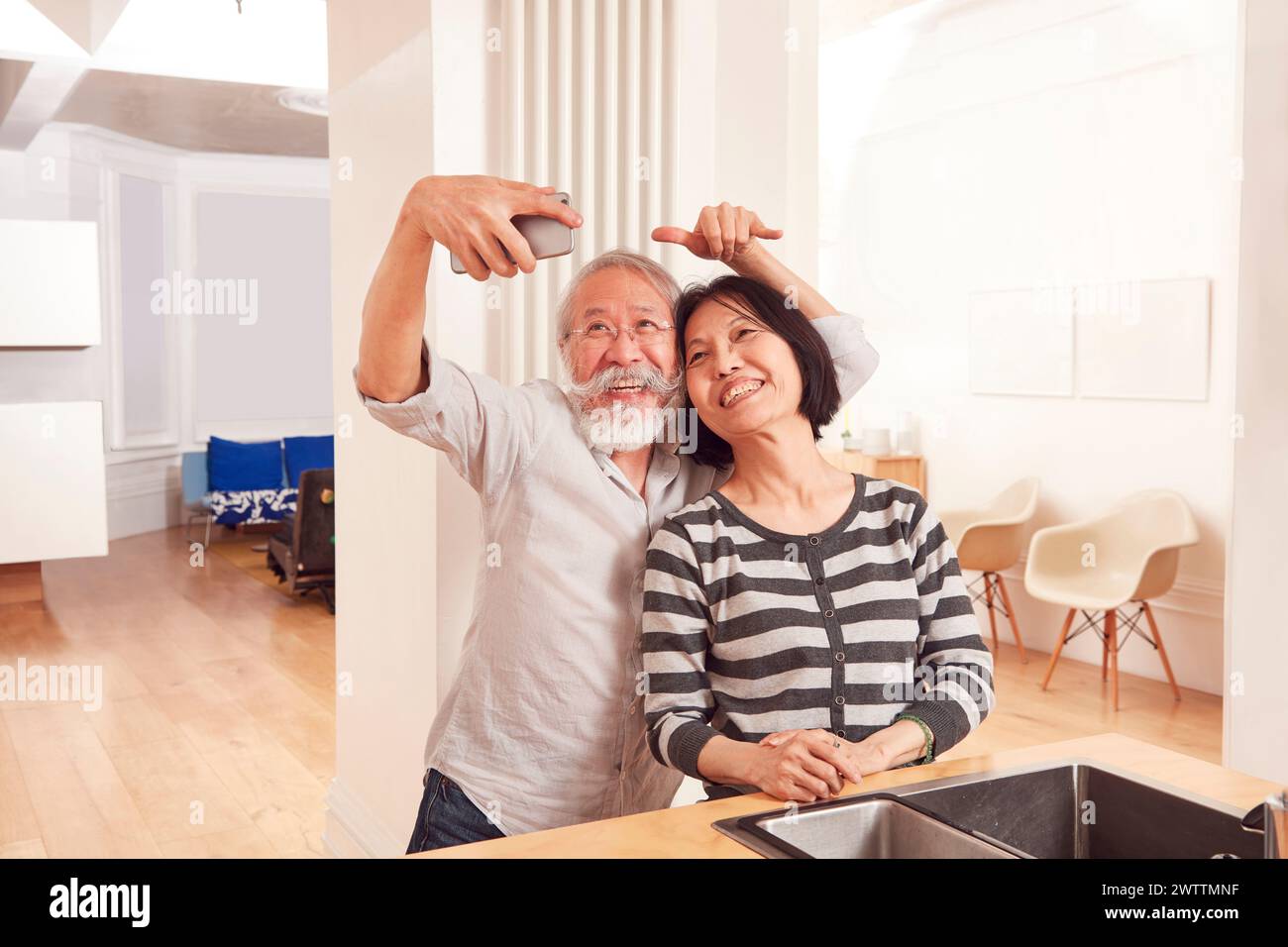 Elderly couple taking a selfie in a bright kitchen. Stock Photo