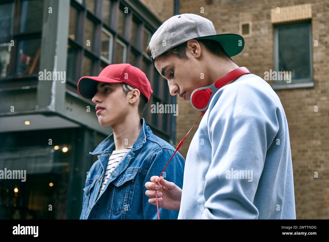 Two young men with headphones and caps standing outside. Stock Photo