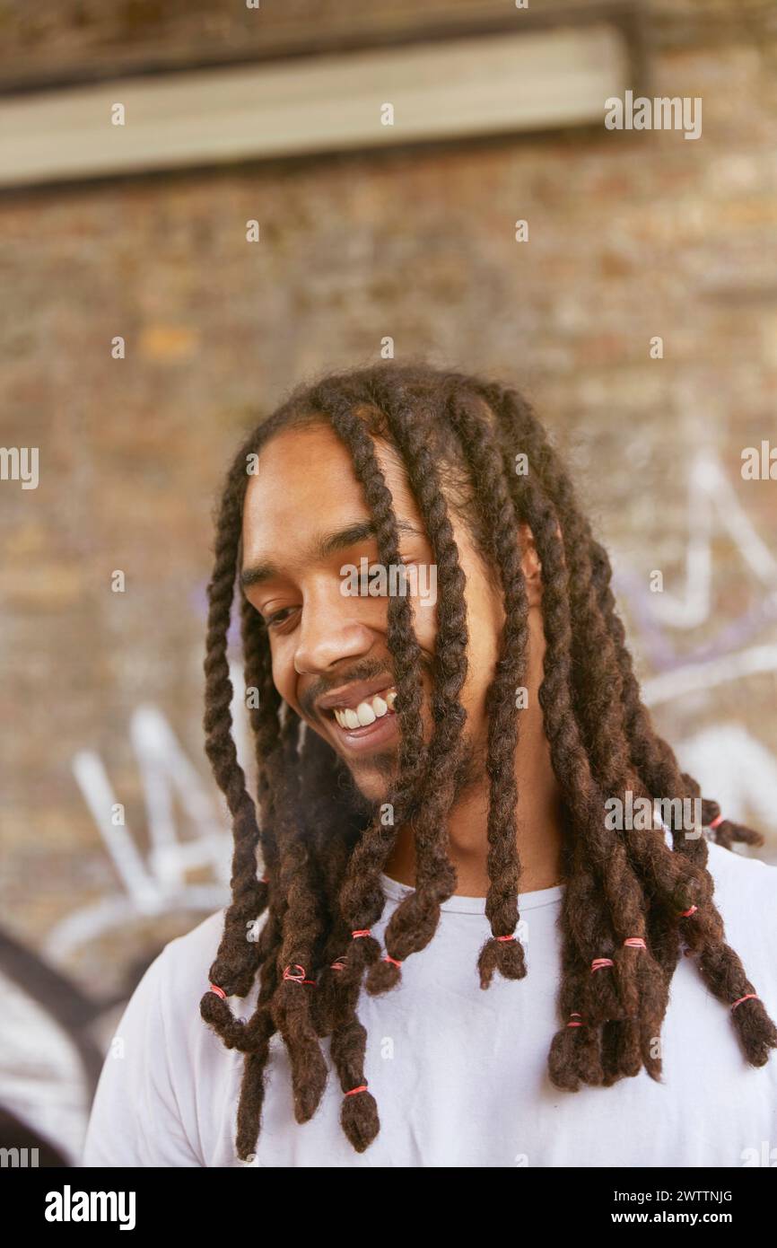 Smiling man with dreadlocks standing against a brick wall Stock Photo