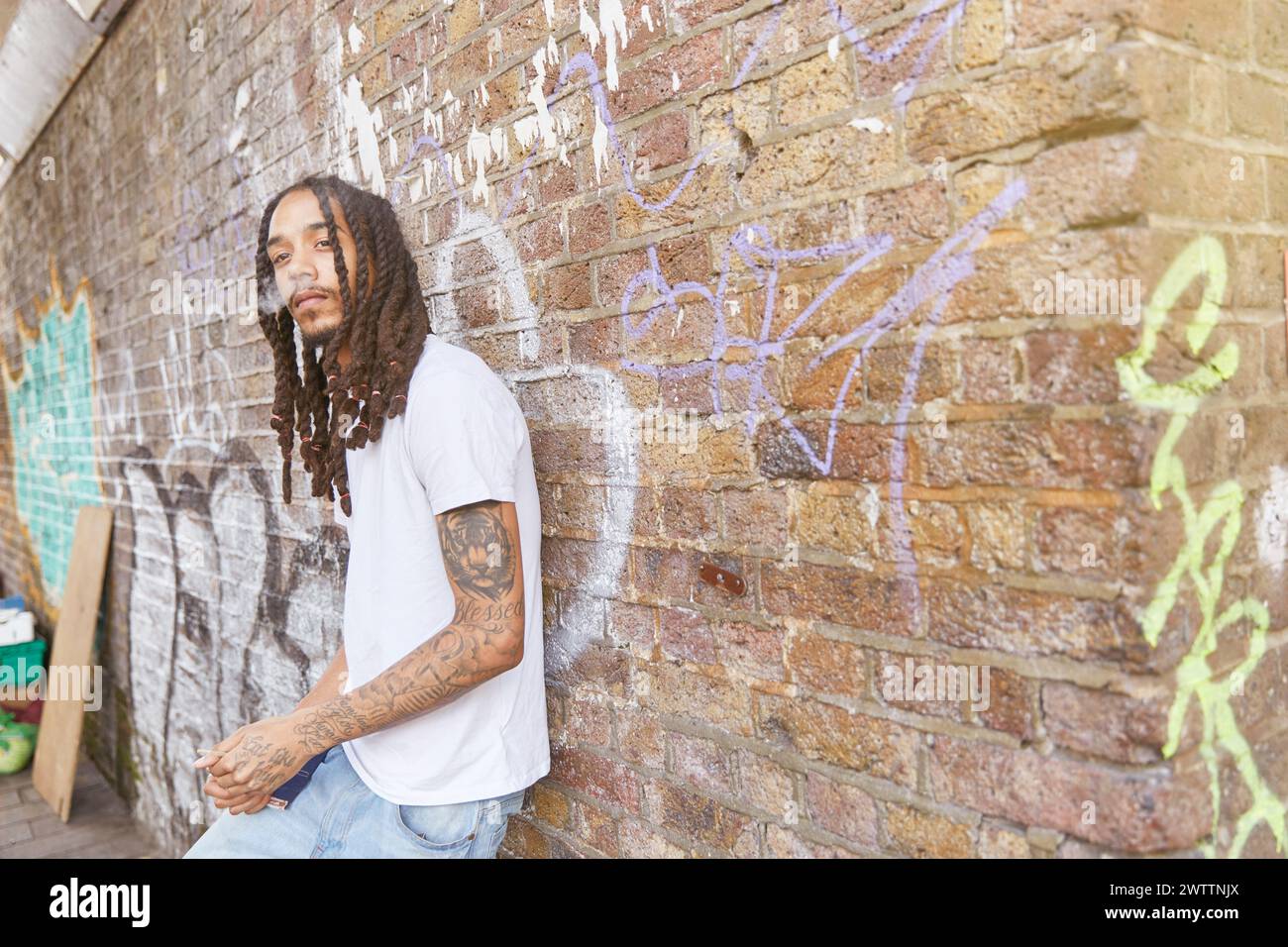 Man leaning against a graffiti-covered wall Stock Photo