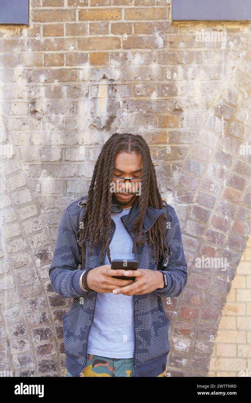 Man using smartphone against brick wall Stock Photo
