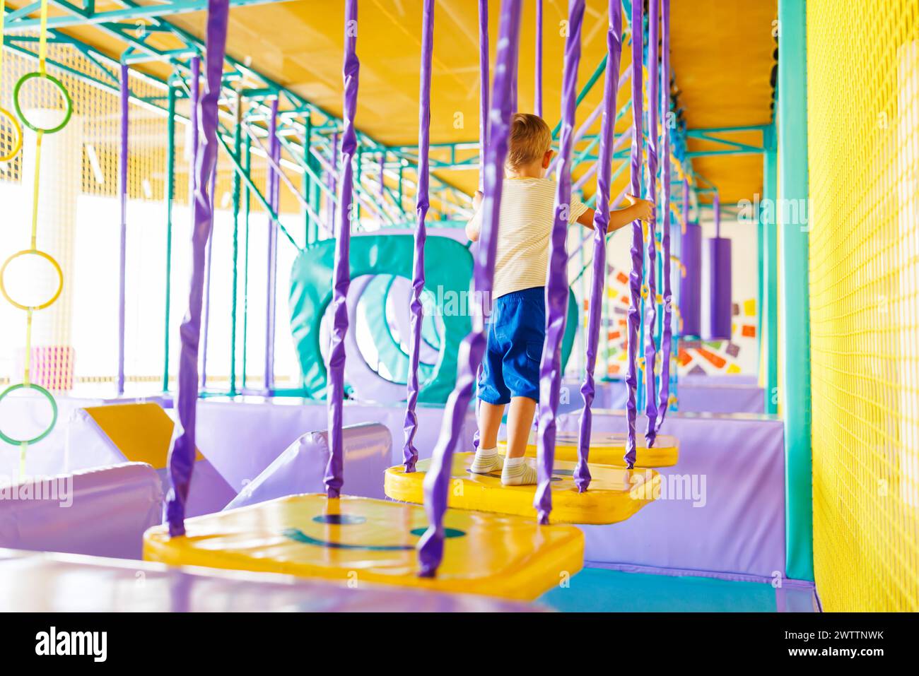 Child navigating through purple and yellow play structure in indoor playground. Stock Photo