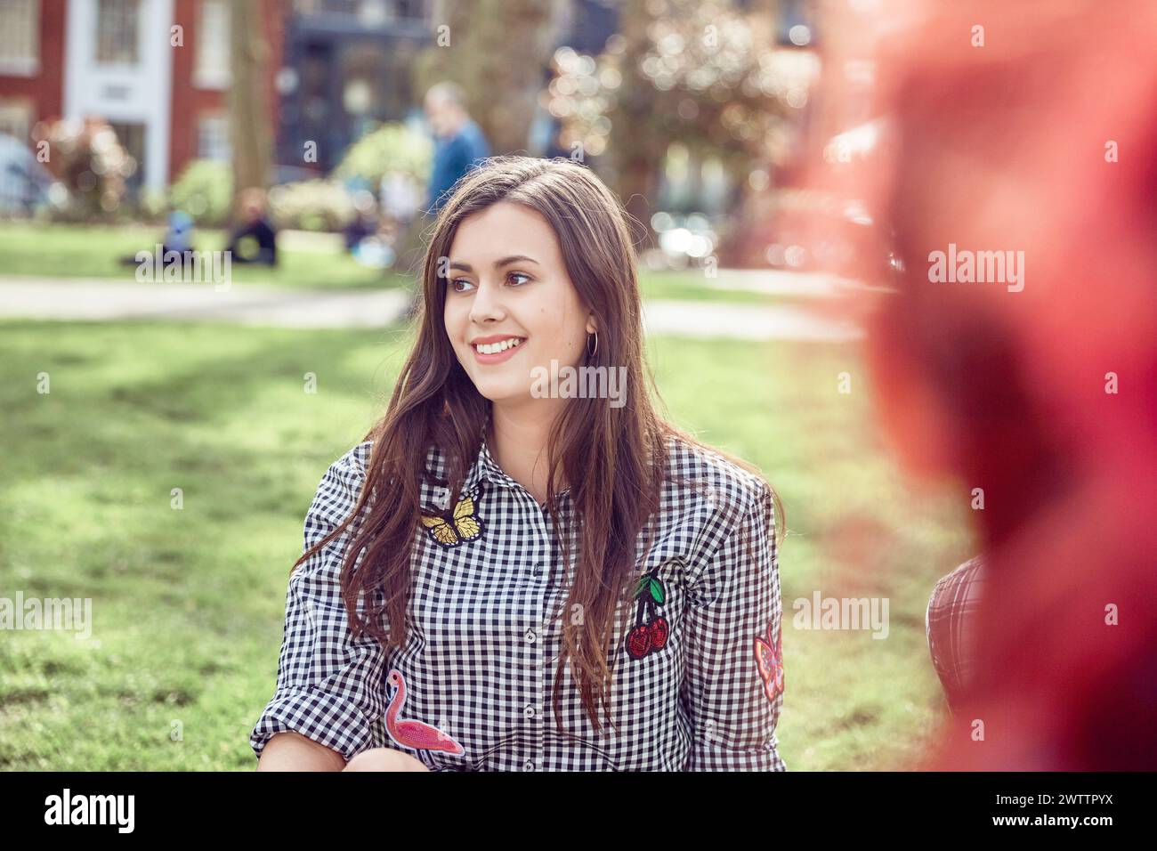 Smiling young woman sitting in a sunny park Stock Photo