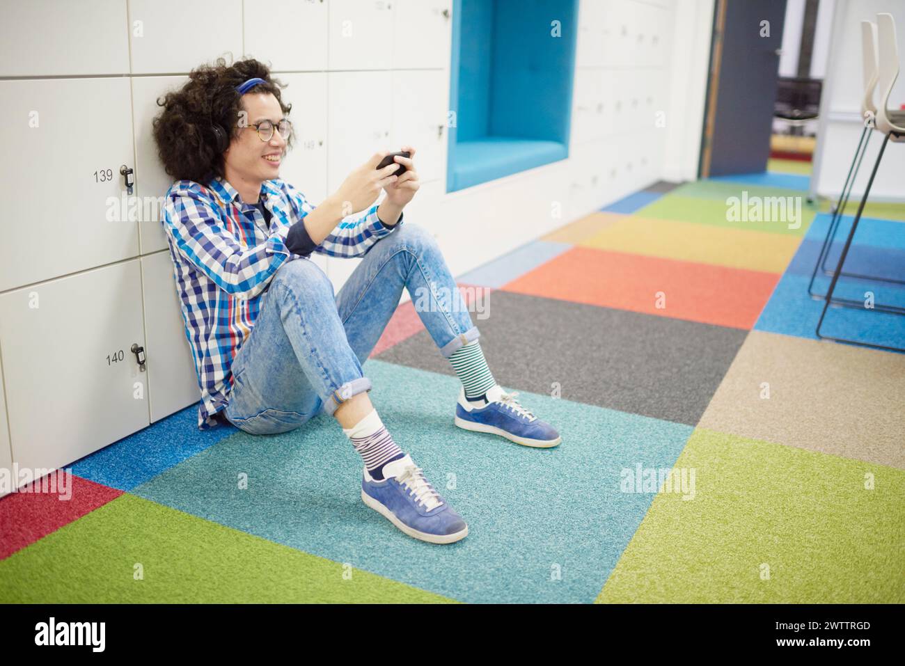 Smiling person sitting on the floor using a smartphone Stock Photo