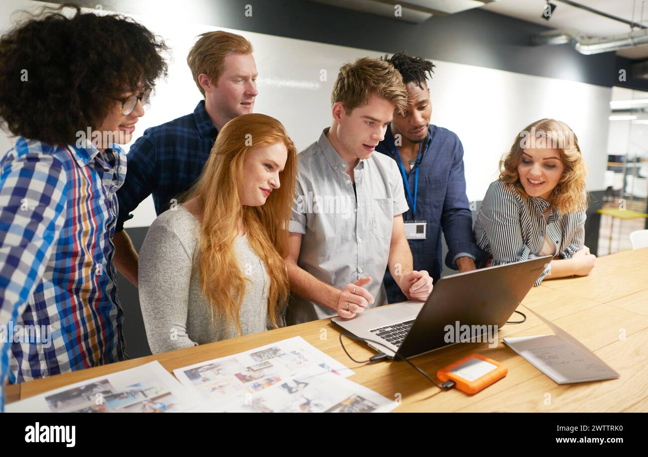 Team of six colleagues collaborating around a laptop Stock Photo