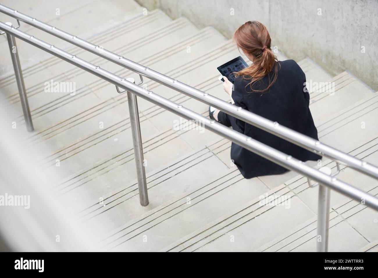 Woman sitting on stairs using a tablet Stock Photo