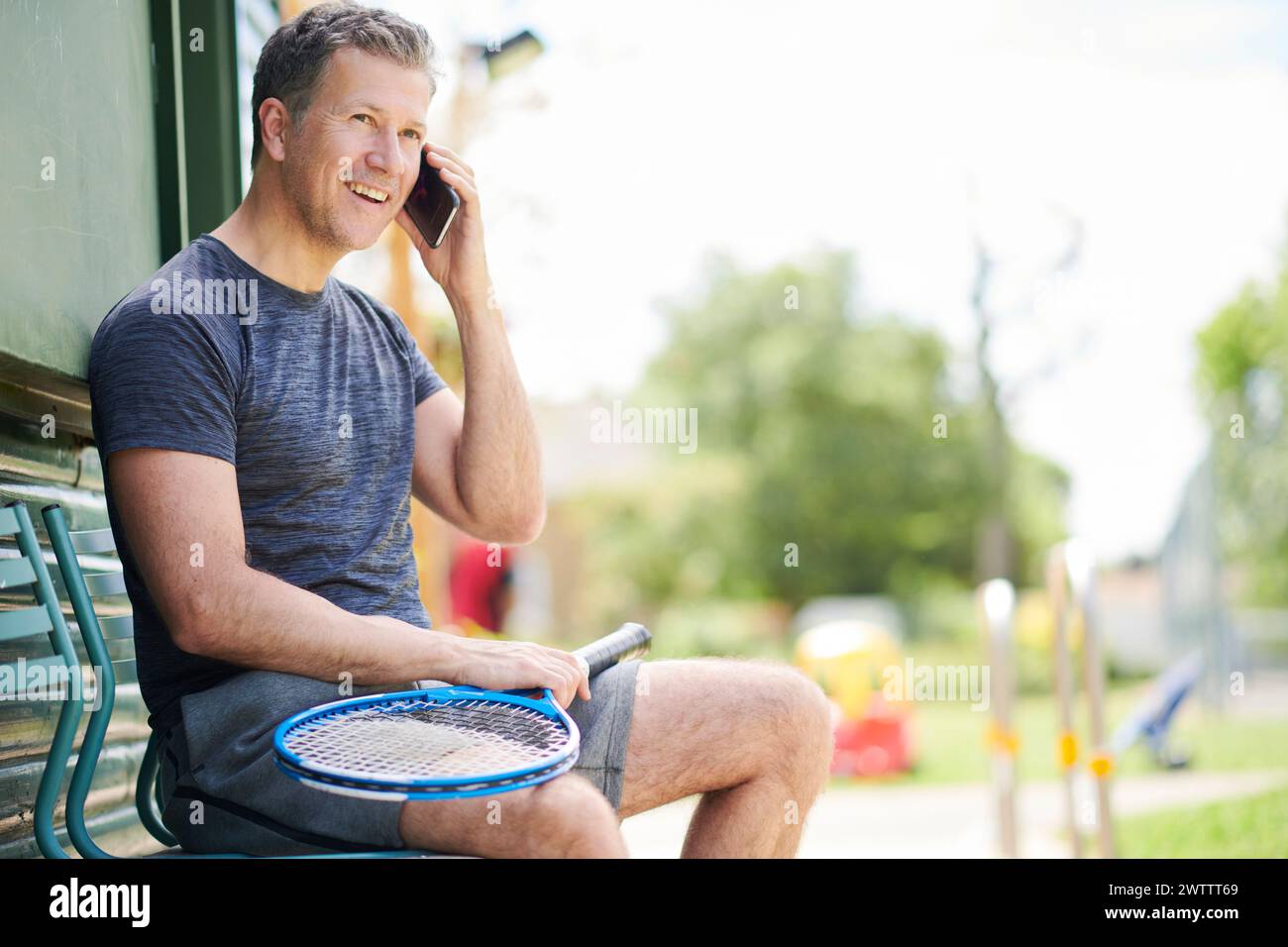 Man talking on the phone while holding a tennis racket. Stock Photo