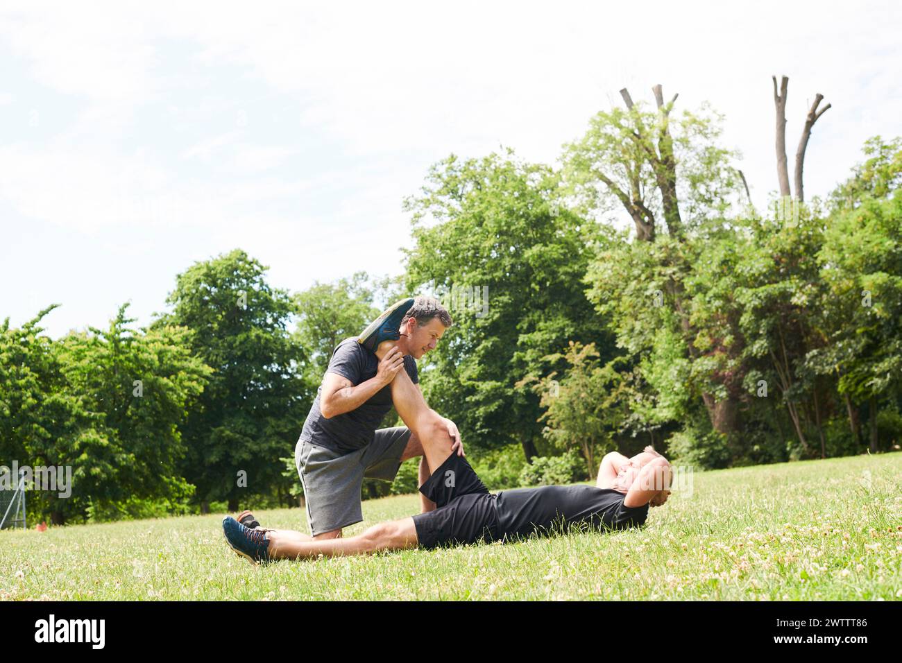 Personal trainer assisting client with stretching exercises in a park Stock Photo