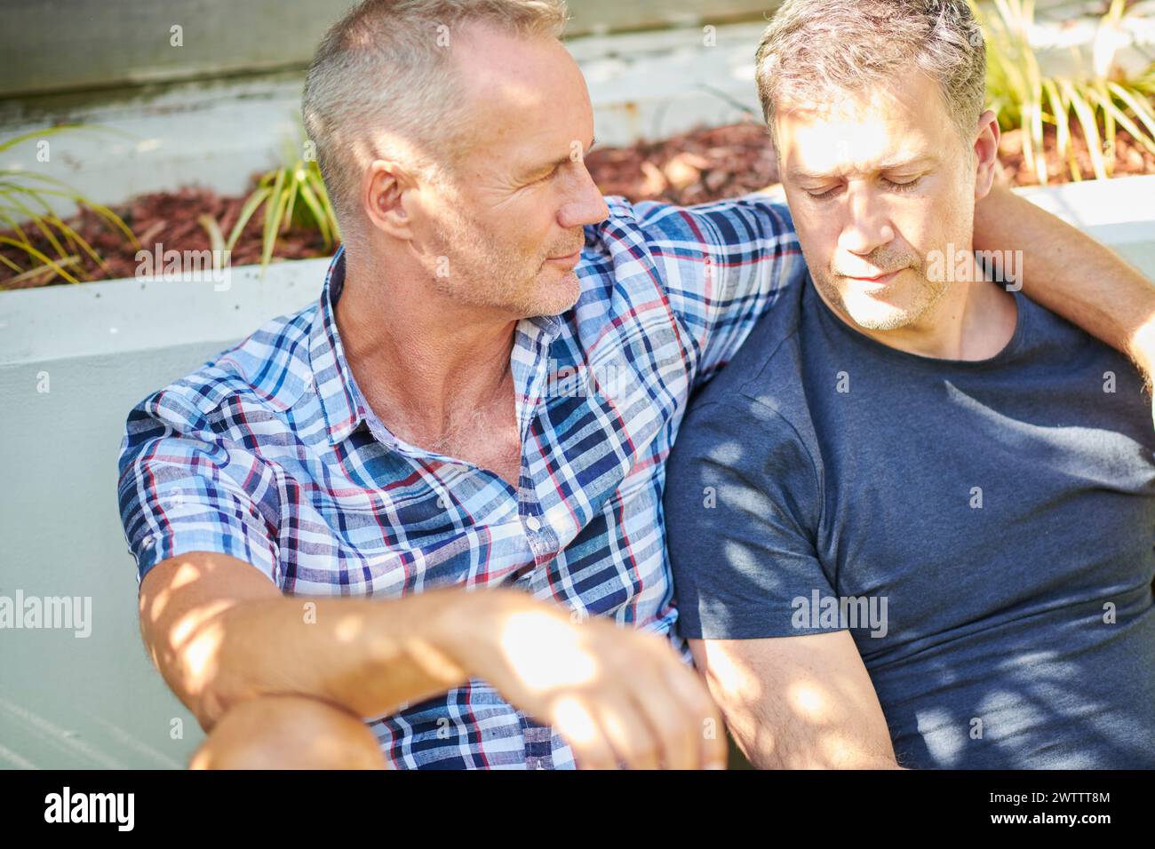 Two men sitting closely on a bench outdoors Stock Photo