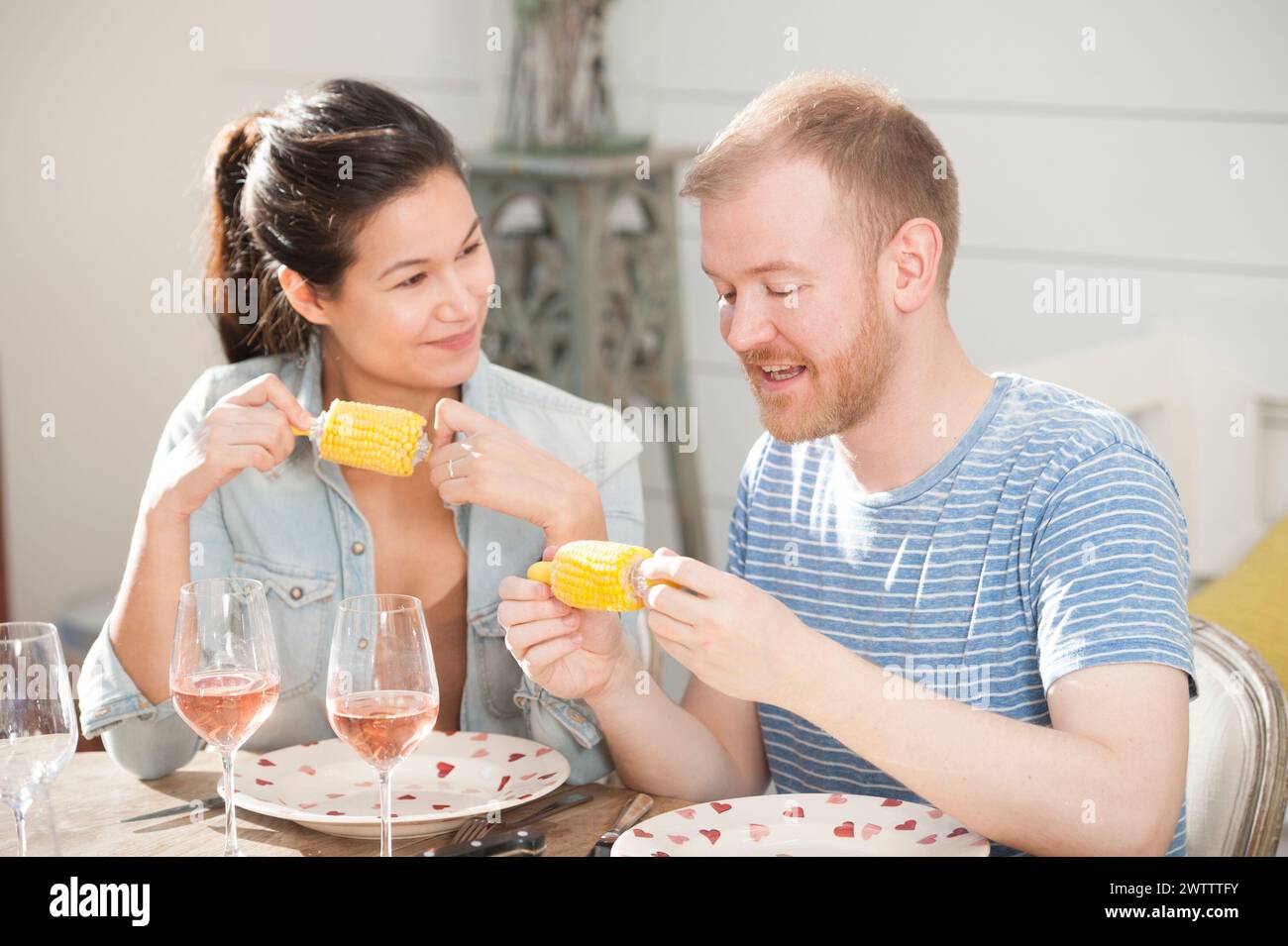 Two people enjoying corn on the cob at a dining table Stock Photo