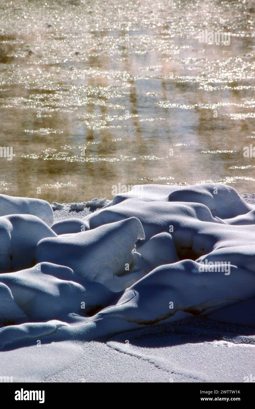 Icy river with mist flowing behind snow covered rocks Stock Photo