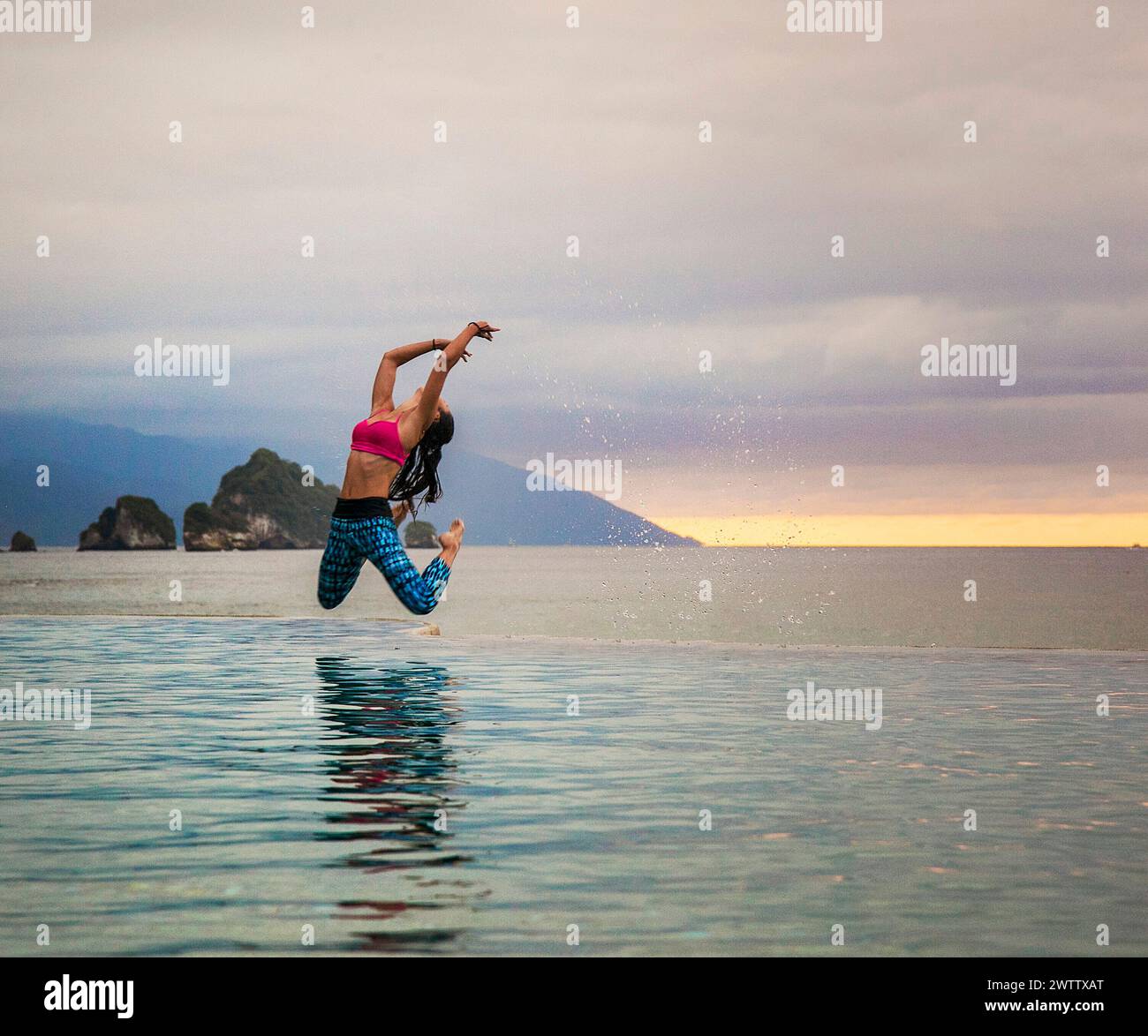 Woman jumping into a serene water body at sunset. Stock Photo