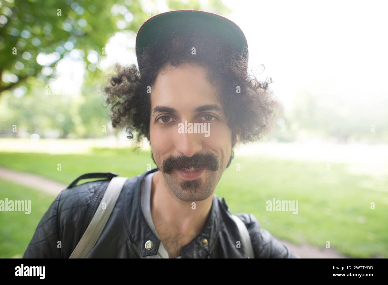 Man with curly hair wearing a cap smiling in a park Stock Photo
