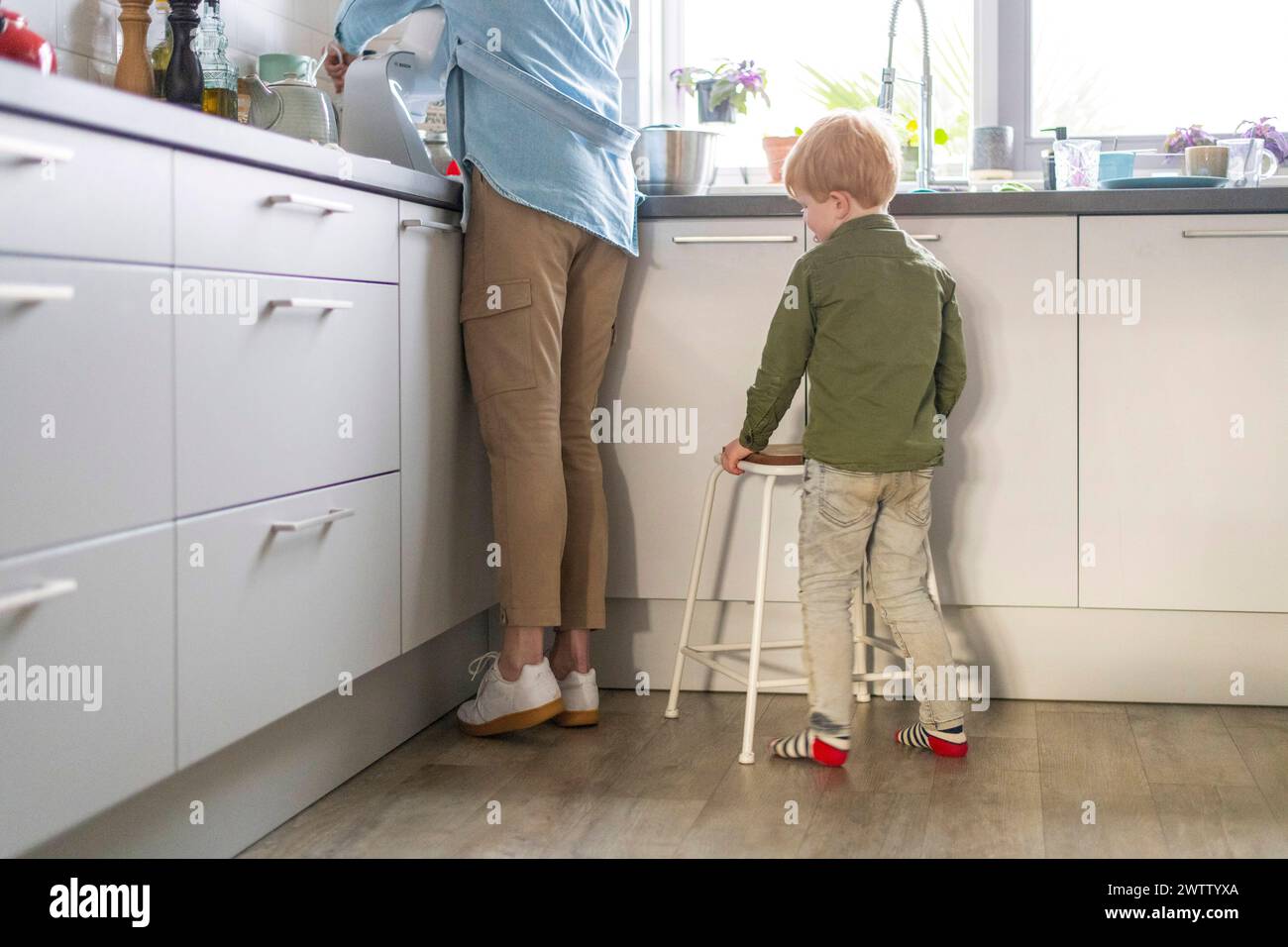 A child helping in the kitchen standing next to an adult at the counter. Stock Photo