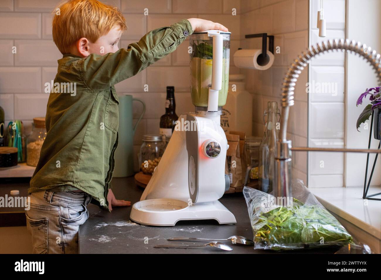 Young boy making a green smoothie in a modern kitchen. Stock Photo