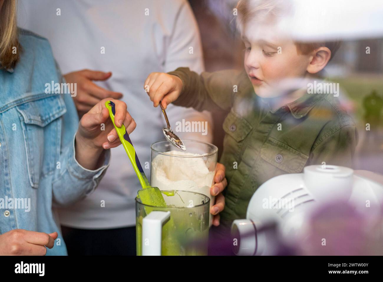 A child helps with cooking, surrounded by family in a home kitchen atmosphere. Stock Photo