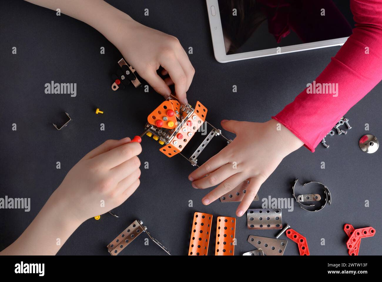 Children piece together robot from small metal parts and screws. Highlighting  learning, teamwork, creativity, and interactive engagement Stock Photo