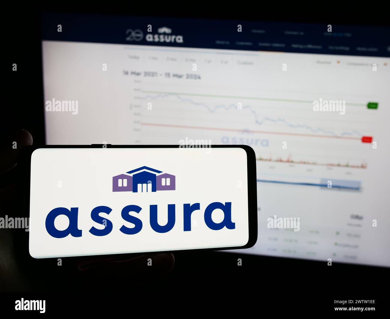 Person holding mobile phone with logo of British healthcare real estate company Assura plc in front of business web page. Focus on phone display. Stock Photo