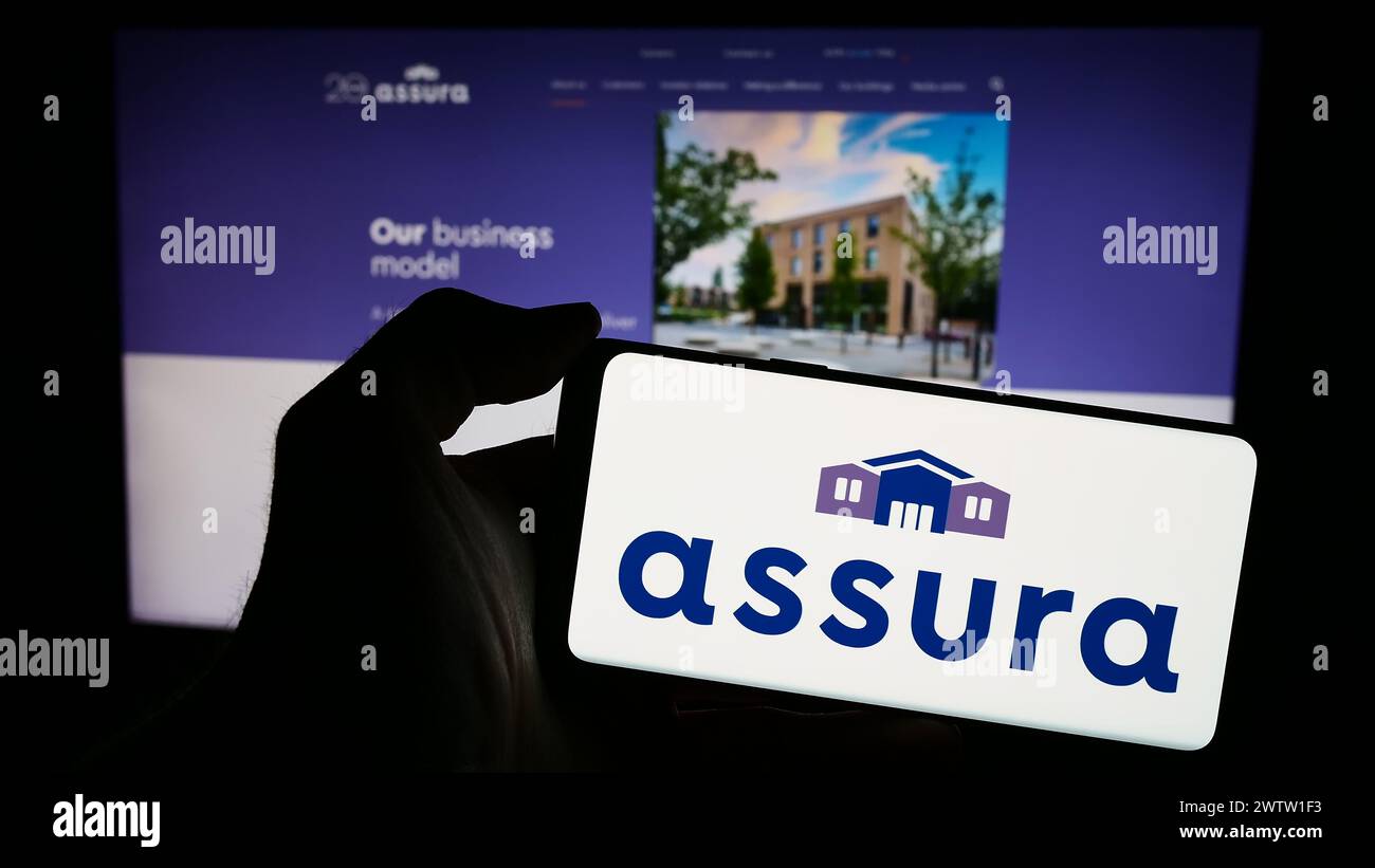 Person holding smartphone with logo of British healthcare real estate company Assura plc in front of website. Focus on phone display. Stock Photo