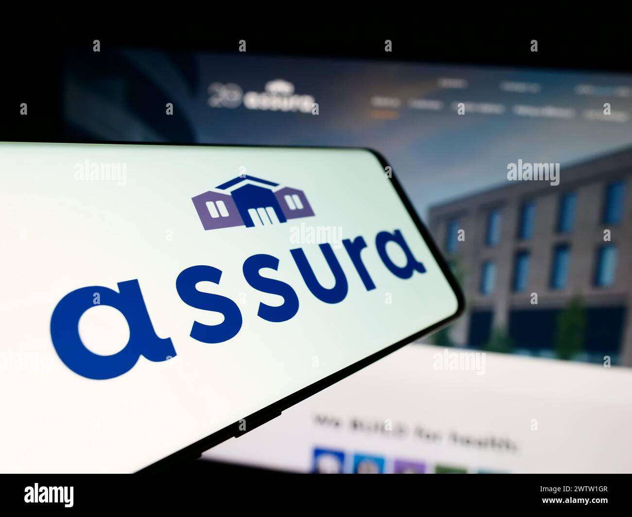 Mobile phone with logo of British healthcare real estate company Assura plc in front of business website. Focus on center-left of phone display. Stock Photo