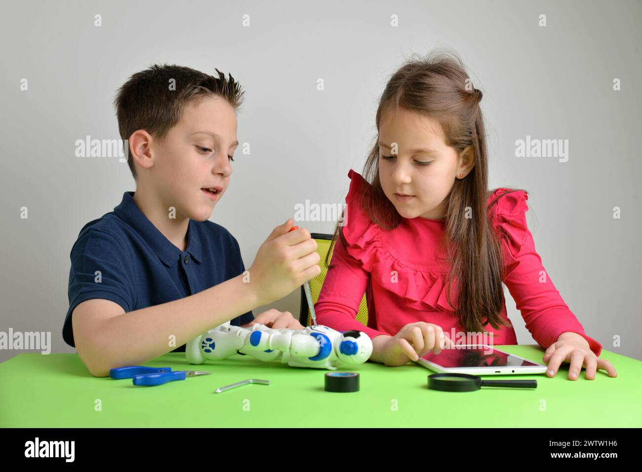 Children assemble robot on work table, engaging in conversation. Concept of teamwork, collaboration, education, and hands-on learning experience Stock Photo
