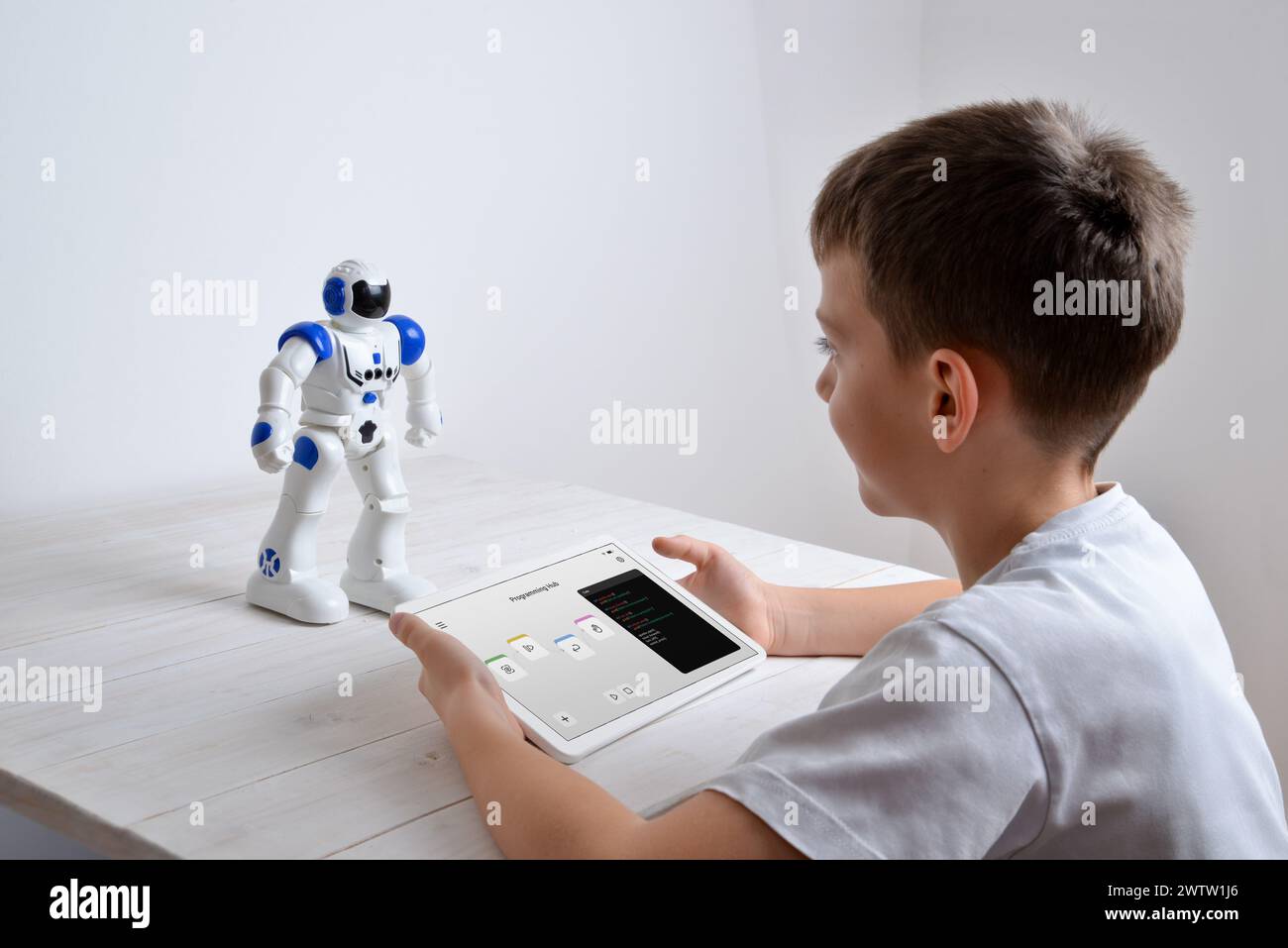 Boy is programming the work of a robot on a desk with a tablet in his hand Stock Photo