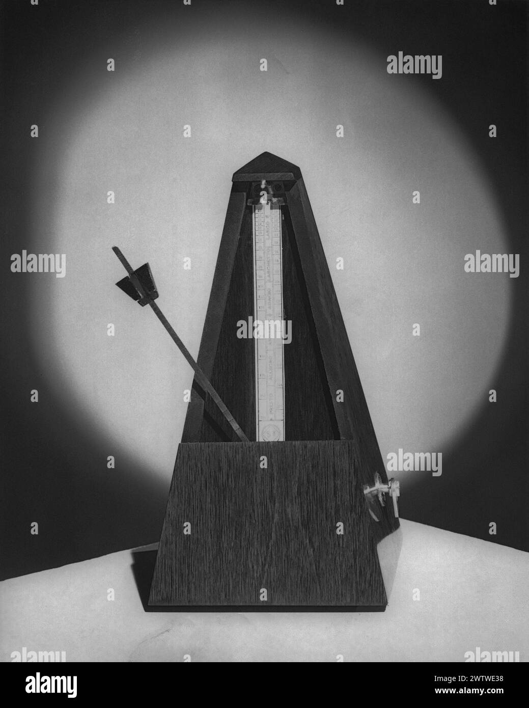 Dramatic image of an old-fashioned wooden metronome sitting on a table with around light shining on the background behind it Stock Photo