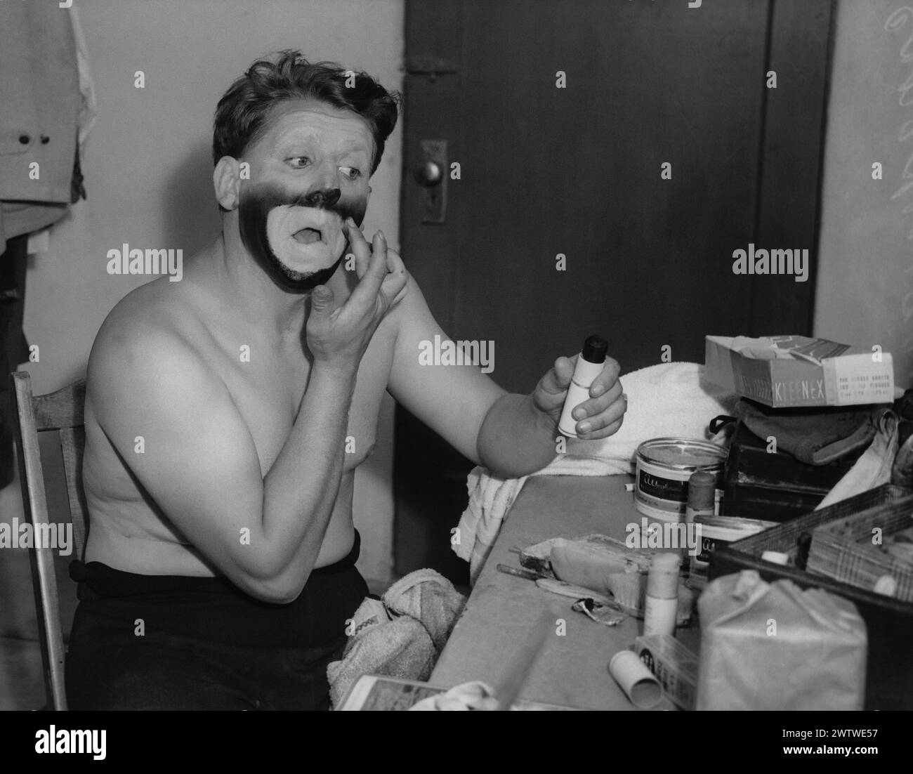 Man sits at a makeup table putting on his makeup to be a clown Stock Photo