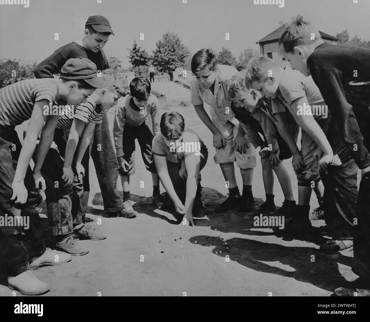 Large group of school age boys in a huddle around a dirt marble pit