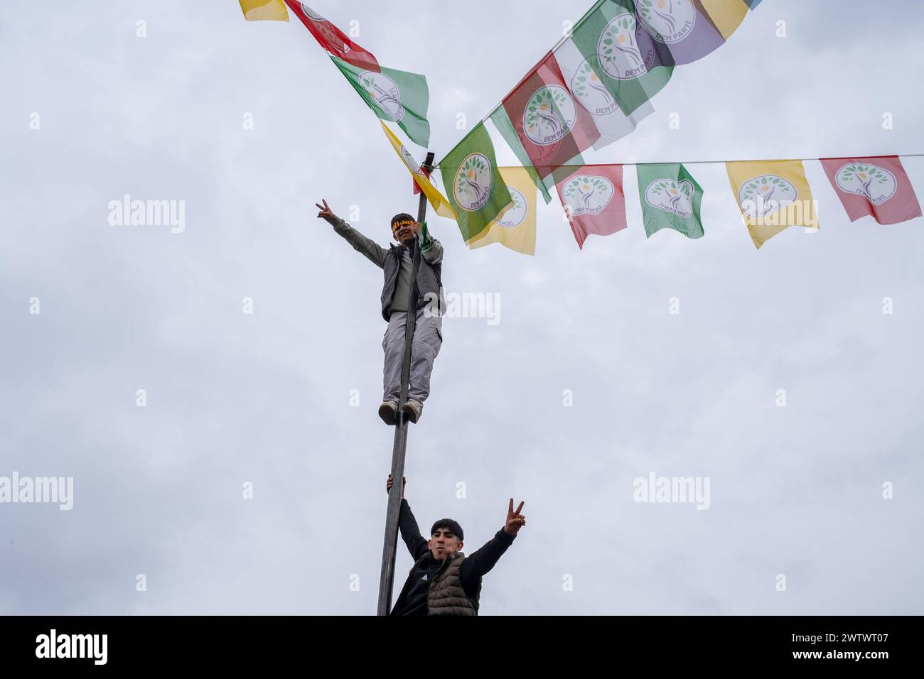 Batman, Turkey. 19th Mar, 2024. Two young people climb the pole with the flags and make a victory sign. Tens of thousands of people gathered in Batman to celebrate the arrival of the new year and spring with great enthusiasm and their colorful costumes. Credit: SOPA Images Limited/Alamy Live News Stock Photo